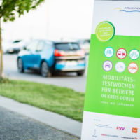 Eine Ladesäule und im Hintergrund ein elektrisch betriebener BMW i3 vor dem Schild der Wirtschaftsförderung im Kreis Düren. E-Mobilität im Unternehmen und Elektromobilitäts-Testwochen im Kreis Düren. Fotograf-Düren-Unternehmensfotografie-Inden-Jülich-Linnich-Langerwehe